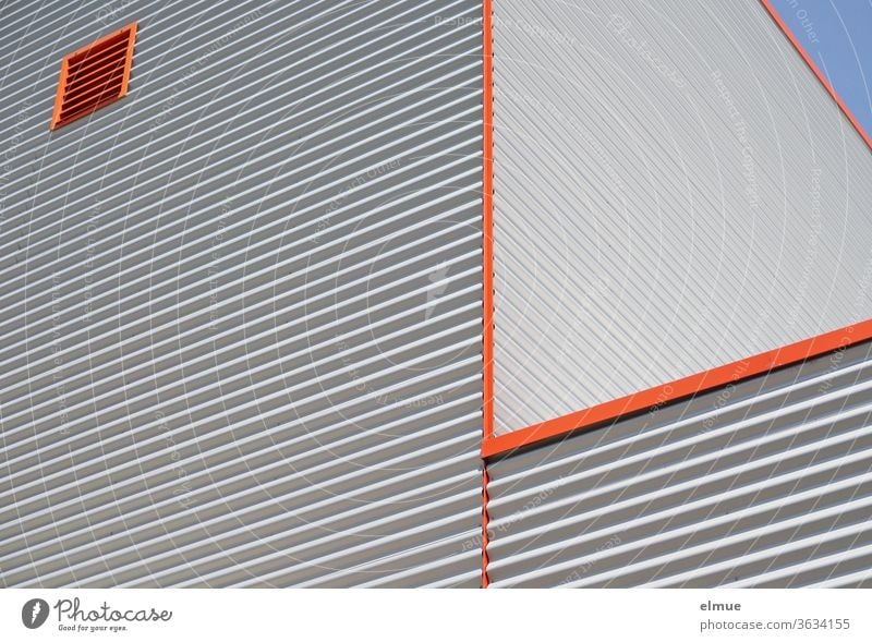 Teilansicht eines in der Höhe abgesetzten Zweckgebäudes aus grauem Wellblech, orangefarbenen Kanten und einem orangefarbenen, quadratischen Lüftungsfenster aus der Froschperspektive