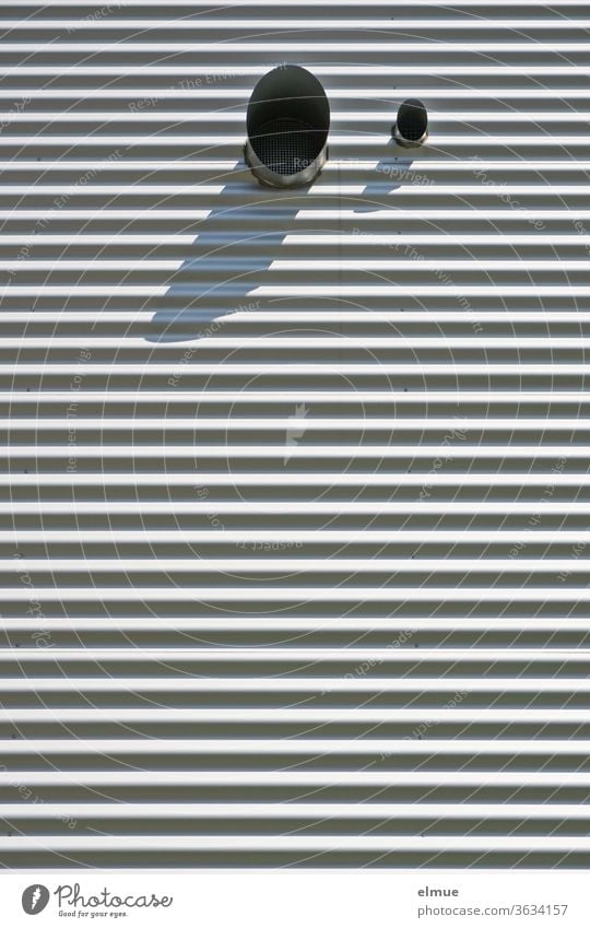 Fassade eines Zweckgebäudes aus grauem Wellblech mit zwei runden Lüftungsrohrausgängen (groß/klein) im oberen Teil, die Schatten werfen Gebäude Wellblechfassade