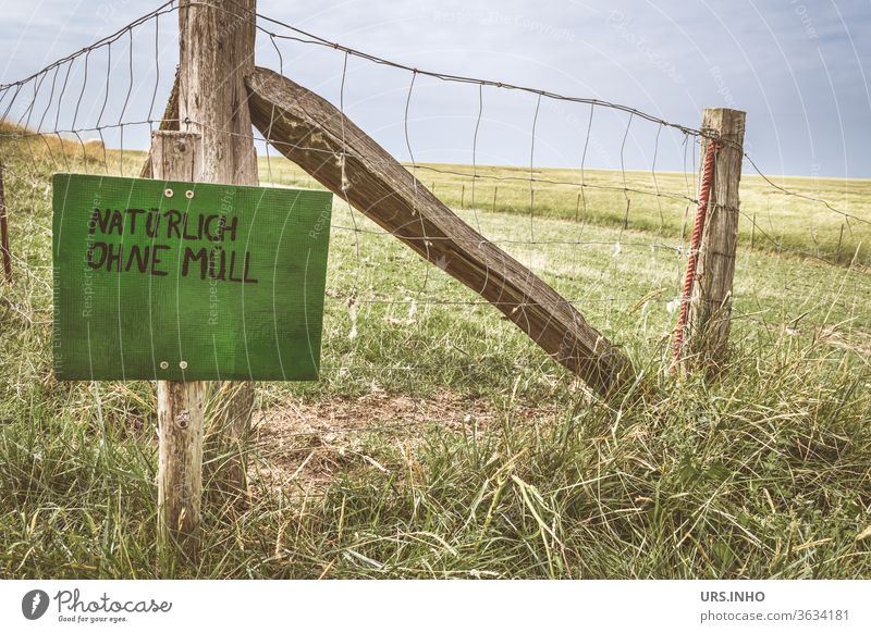 grünes Schild mit der Aufschrift NATÜRLICH OHNE MÜLL an einem Weidezaun Wiese Zaun Schilder & Markierungen Hinweisschild Schriftzeichen Typographie Satz