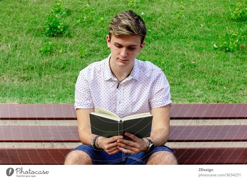 Junger Mann liest ein Buch, während er auf einer Parkbank sitzt Bank männlich jung 1 lesen photogen Erwachsener Person Sommer Schüler Kaukasier Sitzen Freizeit