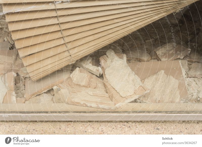 Blick in ein Schaufenster mit defekter Jalousie und Bauschutt als Detail kaputt Renovieren bankrott Steine schief schräg Insolvenz Schutt Trümmer
