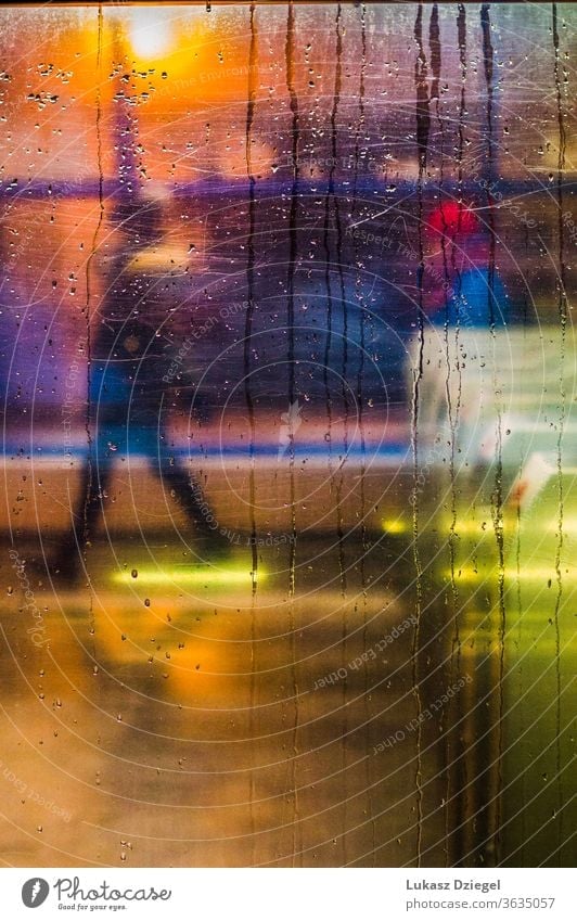 Fenster mit Regentropfen und Stadtlichtern mit einer Person im Hintergrund Nahaufnahme schließen Textur unkenntlich Silhouetten sich[Akk] bewegen