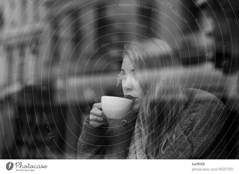 die junge Frau trinkt Kaffee und blickt durch die Scheibe auf die andere Strassenseite Kaffeetrinken Frauengesicht Junge Frau straßenkaffee