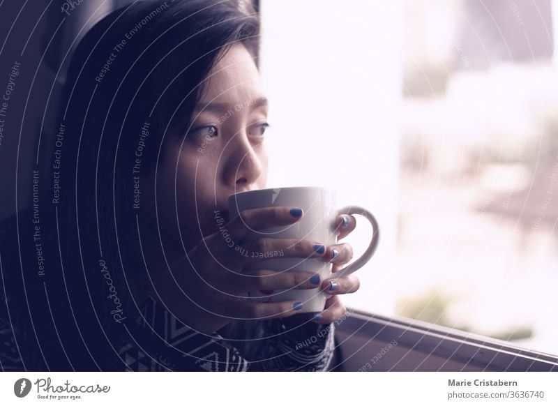 Asiatisches Mädchen, das an einem frühen Herbstmorgen am Fenster Kaffee trinkt, zeigt das Konzept der neuen normalen, häuslichen Quarantäne und Selbstisolierung während der Covid-19-Pandemie