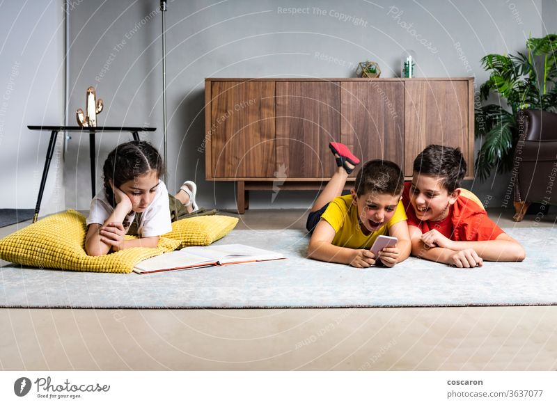 Kleines Mädchen liest ein Buch, während zwei Jungen mit einem Smartphone spielen Brüder Handy heiter Kind Kindheit Kinder Mitteilung niedlich Daten anders