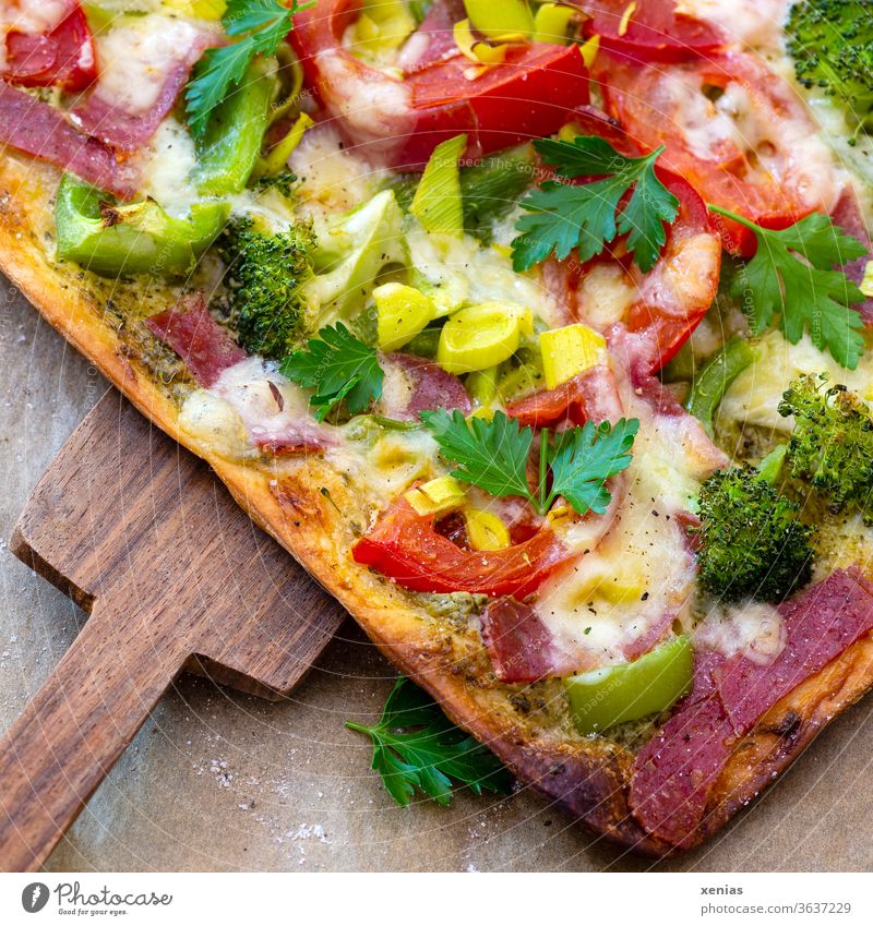Seĺbstgebackene Pizza dick belegt mit Tomaten,  Broccoli, Lauch, Salami und natürlich viel Käse oben drauf. Das große Stück wird mit dem Holzschieber vom Backpapier geholt.