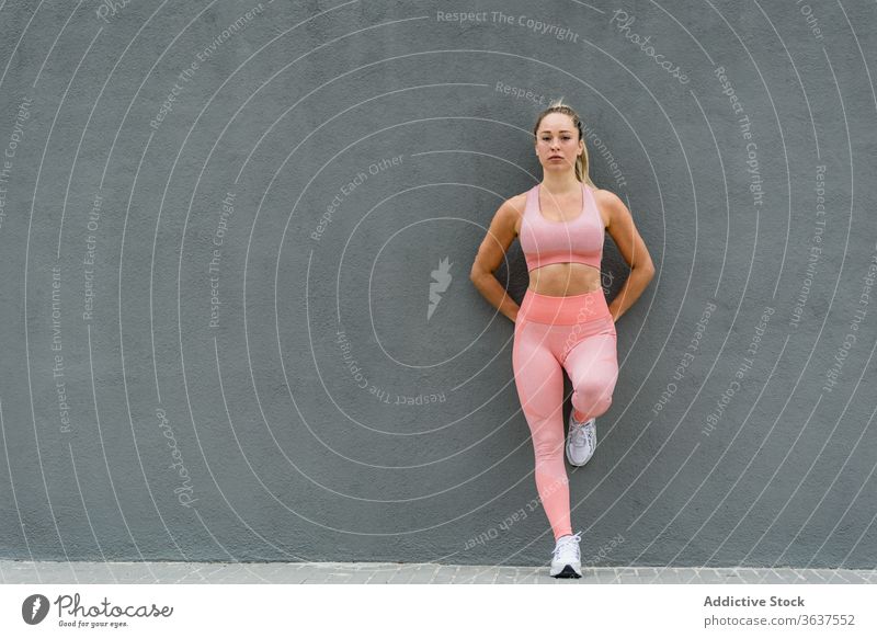 Aktiv getragene Sportlerin an graue Wand gelehnt stehend Bein anlehnen passen Gesundheit Wohlbefinden Sportkleidung Harmonie Vitalität Leggings Turnschuh