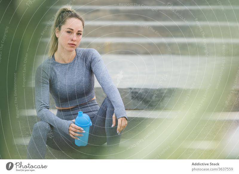 Kontemplative Sportlerin, die sich nach dem Training mit einer Flasche auf einer Treppe ausruht Athlet Pause Wasser Denken beschaulich Gesundheit ruhen