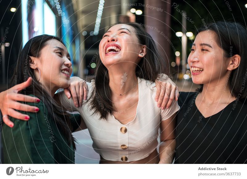 Fröhliche ethnische Frauen reden auf der Straße Unternehmen Lachen Zusammensein Freundin schlendern Großstadt Nacht heiter Humor Freundschaft asiatisch
