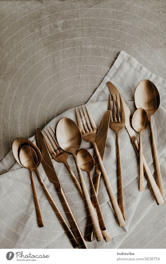 Goldene Besteckkomposition auf grauem Hintergrund - Löffel, Gabel und Messer gold Silberwaren Utensilien Küchengeräte vereinzelt Essen zubereiten Lebensmittel