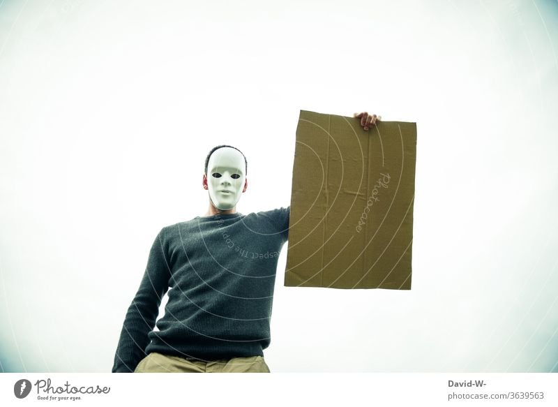 anonym - maskierter Mann hält ein leeres Schild aus Pappkarton in die Luft Karton Pappe anonymous Maske Anonymität pappkarton Hinweis hinweisend Sicherheit