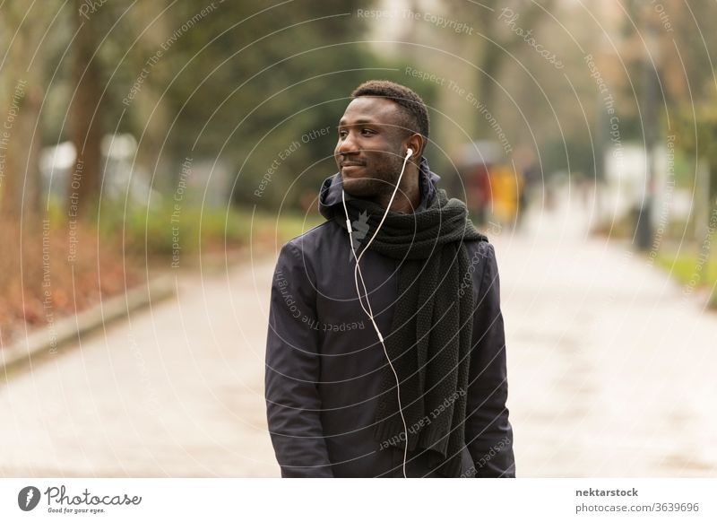 Junger schwarzer Mann mit Kopfhörern schaut weg und geht im Park spazieren Porträt afrikanische ethnische Zugehörigkeit öffentlicher Park hören Musik Hörbuch