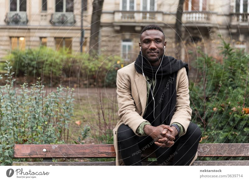 Junger schwarzer Mann sitzt auf der Bank und listet ein Hörbuch auf, das in die Kamera schaut Porträt Kopfhörer afrikanische ethnische Zugehörigkeit