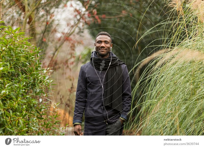 Fröhlicher schwarzer Mann mit Kopfhörern posiert im Park Porträt afrikanische ethnische Zugehörigkeit Herbstblattfarbe Gras hoch öffentlicher Park hören Musik