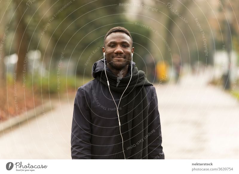Junger Mann lauscht Kopfhörern, die selbstbewusst in die Kamera lächeln Porträt afrikanische ethnische Zugehörigkeit schwarz öffentlicher Park Straße Nachlauf