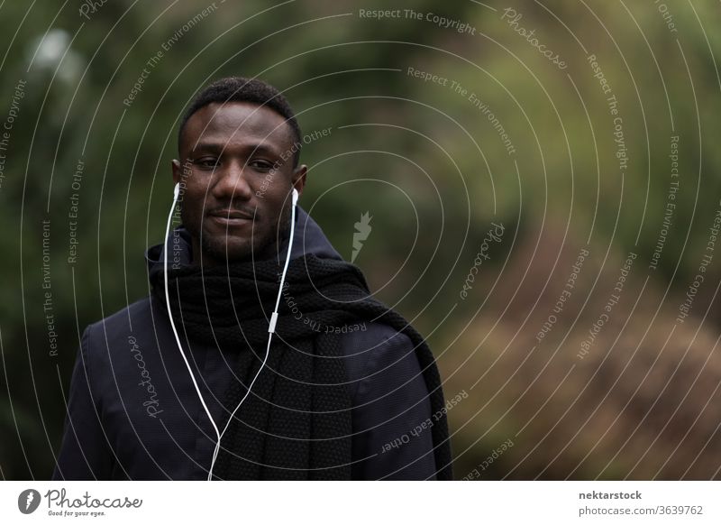 Porträt eines jungen schwarzen Mannes, der im Park Kopfhörer hört afrikanische ethnische Zugehörigkeit öffentlicher Park hören Musik Hörbuch
