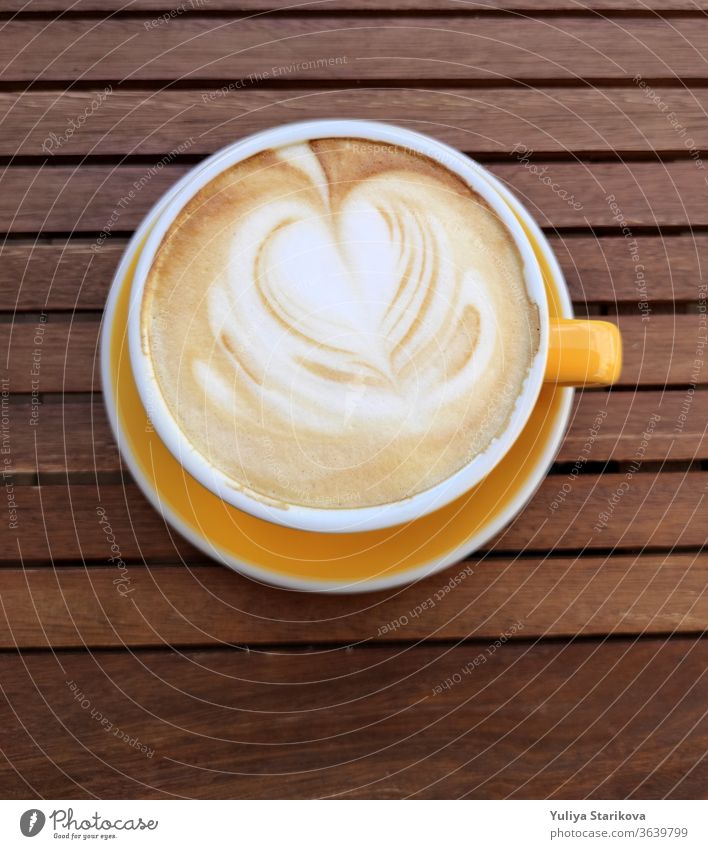 Gelbe Tasse Kaffee mit Milch auf dunklem Hintergrund. Heißer Latte oder Cappuccino mit Schaum mit Herz auf einem Holztisch mit Kopierraum. Ansicht von oben.