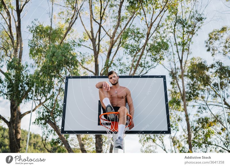 Basketballspieler sitzt auf einem Korb auf dem Spielplatz Reifen Mann Sportler Spieler Training Gesundheit männlich gutaussehend professionell Aktivität Übung