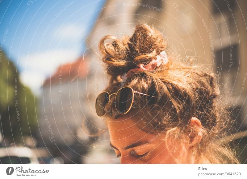 Eine junge Frau mit Sonnenbrille und Dutt im Haar in der Sonne Haare Sommer Sonner sommerlich Sonnenschein Urlaubsstimmung Frisur hochgesteckt Knoten Haarknoten