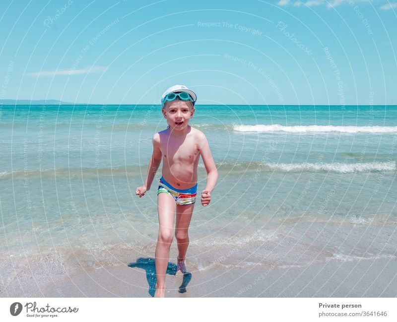 Glücklicher kleiner lächelnder Junge läuft an einem sonnigen Sommertag am Meeresufer entlang Ufer MEER Strand Sonne Himmel blau jung Lifestyle Sand im Freien