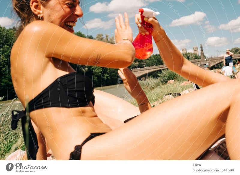 Zwei junge Frauen beim Baden, die Spaß haben und sich mit Wasser aus einer Sprühflasche bespritzen Sommer abkühlen Mädchen sonnen Bikini Sonne Wasserschlacht
