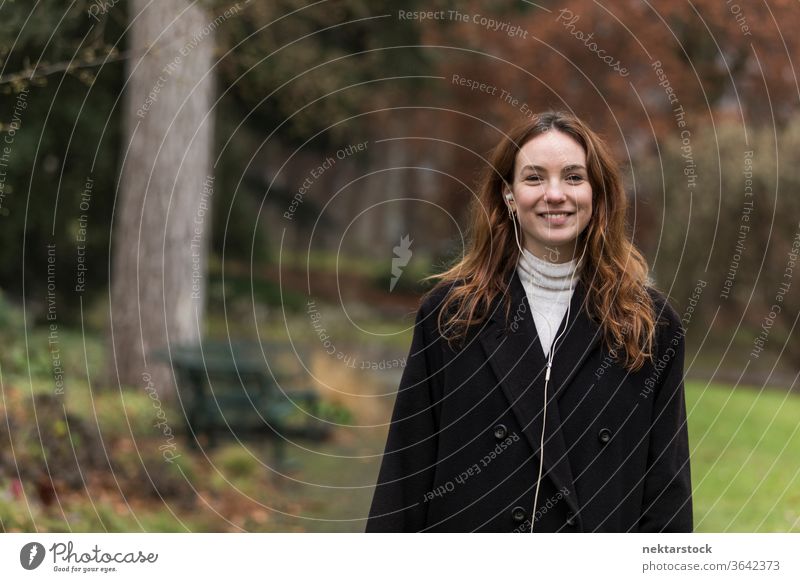 Junge Frau mit zahnbeinigem Lächeln posiert im Autumnal Park kaukasische Ethnizität Kopfhörer Audio Musik hören braune Haare Modell aus dem wirklichen Leben
