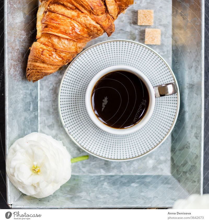 Frisches Croissant, Tasse Kaffee und Hahnenfußblüten. Frühstück Morgen Gebäck weiß Tisch Ranunculus Blumen trinken Tablett Espresso süß schwarz Cappuccino