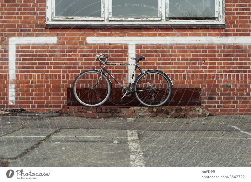 das alte Rad wartet auf Abholung - wobei es das triste Umfeld visuell erheblich bereichert. Fahrrad Fahrradständer Fahrradfahren parken Parkplatz grau 1 Reifen
