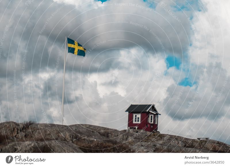 Eine traditionelle rot-weiße kleine Hütte neben der schwedischen Flagge in den südlichen Schären von Göteborg, Schweden Inselgruppe baltisch schön Schönheit