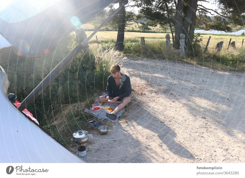 junger Mann sitzt auf einem Feldweg und bereitet eine Picknickpause vor on the road again Ferien & Urlaub & Reisen unterwegs Weg Freiheit Freizeit & Hobby