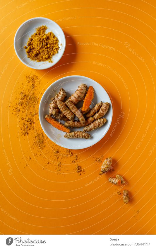 Kurkuma Wurzeln in einer Schüssel und Pulver auf einem orangen Hintergrund. Draufsicht, gesunde Ernahrung. gelb Curcuma Kräuter & Gewürze Farbfoto