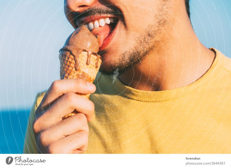 junger Mann in Gelb leckt sein Schokoladeneis blau Nahaufnahme farbenfroh Zapfen cool Sahne cremig essen Essen genießen genießend Genuss Freiheit Spaß lustig