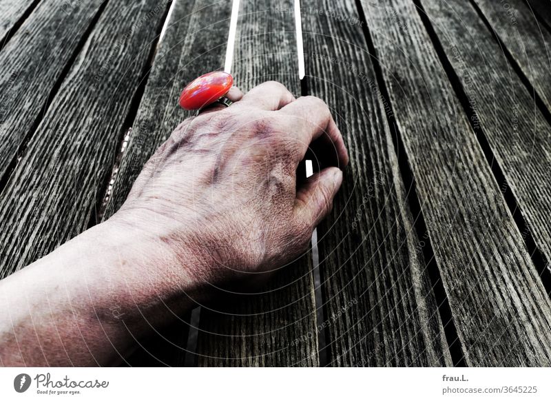 Obwohl mit schickem roten Ring geschmückt, wartet die alte Frau im Kaffegarten vergeblich auf ihr Rendezvous. Hand Bistrotisch Café Schmuck verkrampf Holztisch