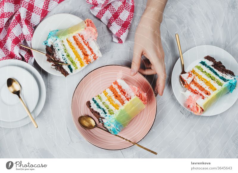 Flächige Lage von regenbogenfarbigen veganen Kuchenstücken auf grauem Hintergrund Frau Mädchen Finger Hände Bäckerei Geburtstag blau hell Feier Schokolade