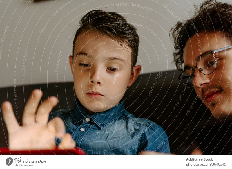Schuljunge mit Bruder blättert auf einem bequemen Sofa Geschwister Junge Tablette benutzend Apparatur Zeitgenosse sich[Akk] entspannen ruhen Browsen Talkrunde