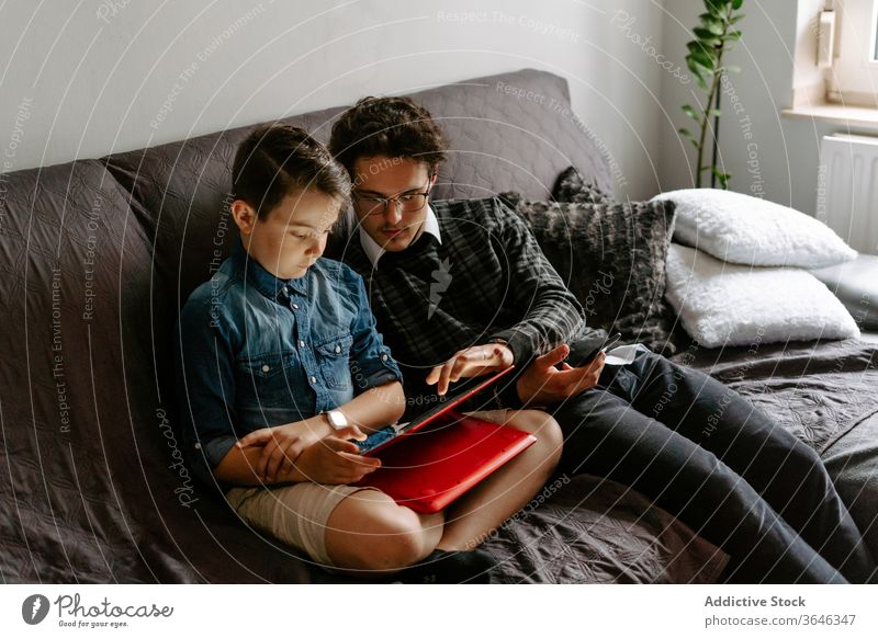 Schuljunge mit Bruder blättert auf einem bequemen Sofa Geschwister Junge Tablette benutzend Apparatur Zeitgenosse sich[Akk] entspannen ruhen Browsen Talkrunde