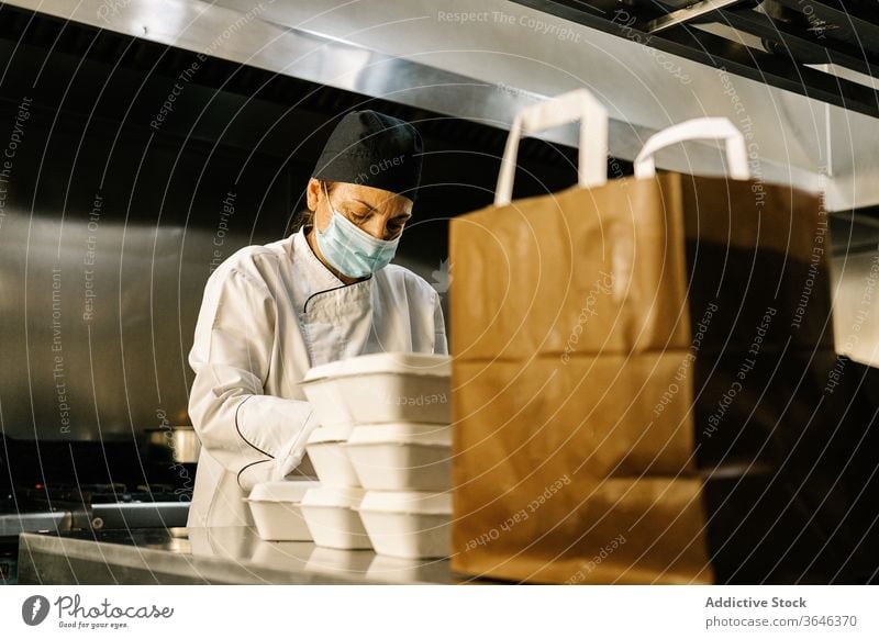 Fokussierte Köchin mit Atemschutzmaske packt Essen zum Mitnehmen Frau Küchenchef Atemschutzgerät Rudel Imbissbude Konzentration Tüte Restaurant Coronavirus