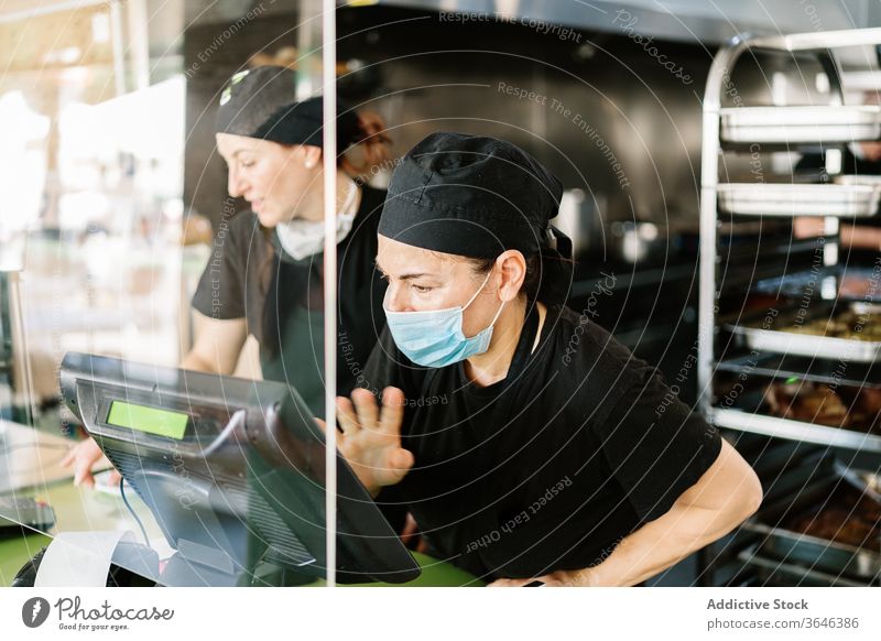 Konzentrierte weibliche Kassiererin mit Gesichtsmaske, die mit der Kasse arbeitet Frauen Arbeit Atemschutzgerät Abfertigungsschalter Café Coronavirus