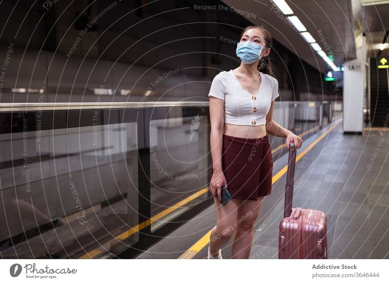 Stilvolle Asiatin mit Atemschutzmaske und Koffer wartet auf den Zug Frau Bahnhof Spaziergang reisen Atemschutzgerät stehen Podest Coronavirus Passagier Bund 19