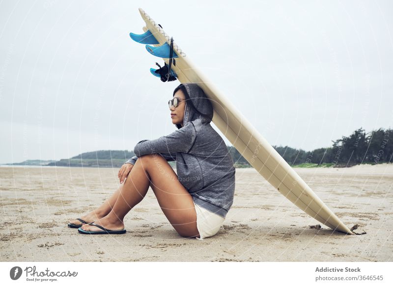 Entspannte Frau sitzt am Strand mit einem Surfbrett auf dem Kopf Surfer ruhen lässig Sand sich[Akk] entspannen sportlich ruhig Sonnenbrille Lifestyle Natur