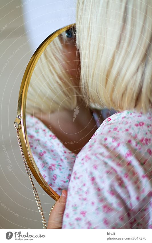 Blondes Mädchen hält zuhause, in heller Wohnung, einen goldenen Spiegel in der Hand und betrachtet, identifiziert neugierig ihr Spiegelbild. Kindliche, spielerische Selbstbetrachtung, Wahrnehmung. Blaues Auge von einem Kind im Spiegel mit Goldrahmen. Zwei.