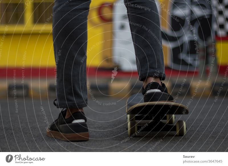Ein junger Mann steht, während er seinen Fuß auf einem Skateboard hält. Skateboarding Sommer neue Normale Sport Freizeit Lifestyle Turnschuh im Freien