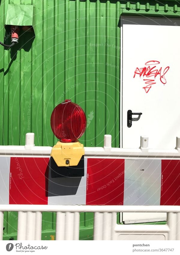 Eine rot-weiß gestreifte Sperre mit Lampe  vor einer Baustelle  mit grünem Container , der mit  einem Graffiti  beschmiert ist. Bauarbeiten. Schutz vor Unfällen
