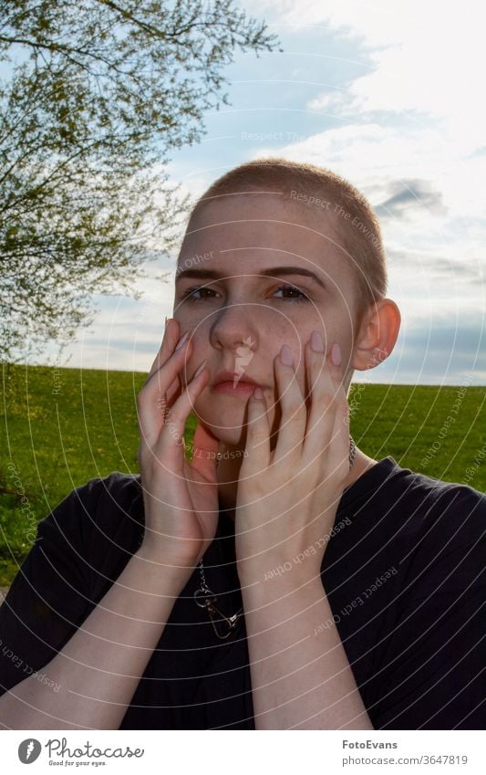 Junge Frau mit sehr kurzem Haar, Hände im Gesicht, steht in der Natur Porträt krank Medizin Mode Tag Schönheit Nägel Krebs attraktiv Mädchen Therapie wirklich