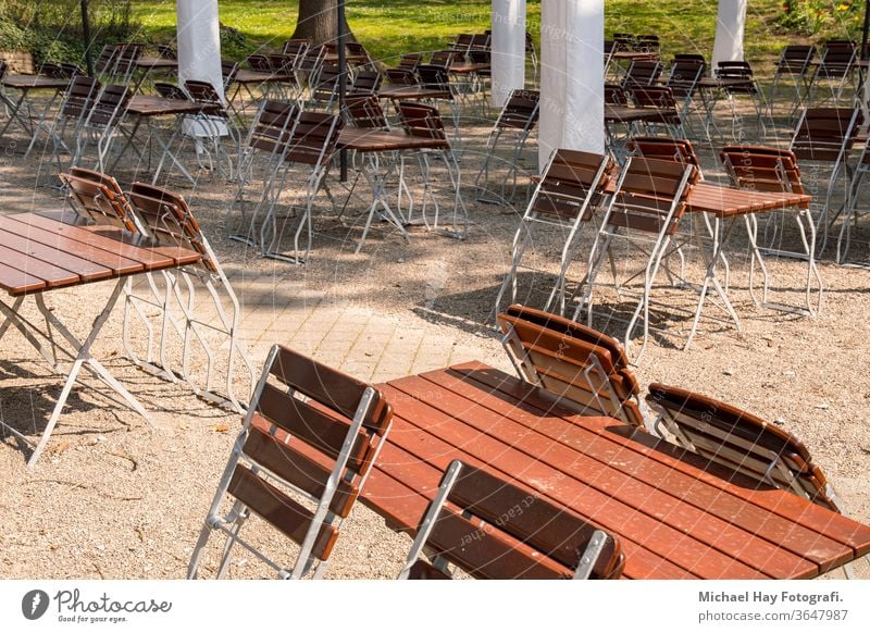 leere Stühle und zusammengeklappte Tische in einem Biergarten Korona Krise Verhaltensregeln Regeln Ausgehverbot soziale Distanz Restaurant Sonnenschirme