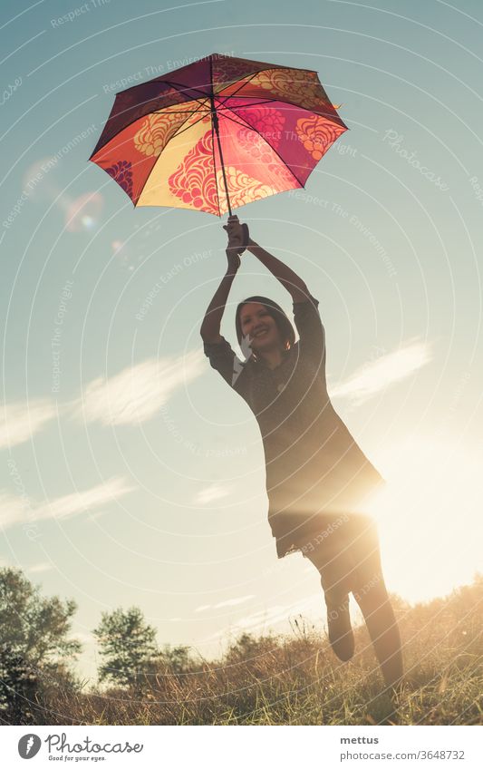 Ein junges körperpositives Mädchen tanzt bei Sonnenuntergang mit einem farbigen Regenschirm auf einer von der Sonne beleuchteten Wiese. Frau Freiheit Glück frei