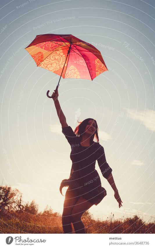 Fröhliche Dame tanzt fröhlich mit rotem Regenschirm im Licht des Sonnenuntergangs auf den Feldern. Frau Freiheit Glück frei Kleid Emotion klassisch Person Bild