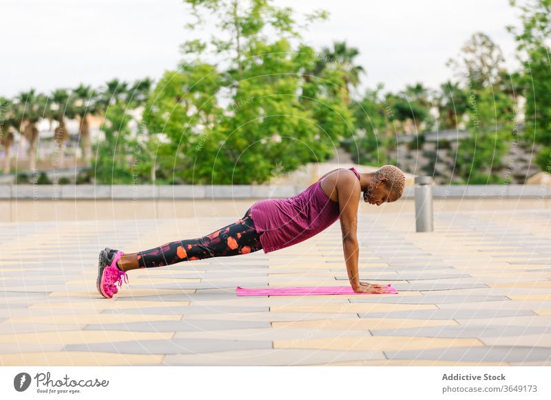 Passgenaue afroamerikanische Frau steht in Ein-Bein-Brett-Pose üben Yoga einbeinige Plankenhaltung Energie Gleichgewicht Ausdauer Konzentration Sportbekleidung