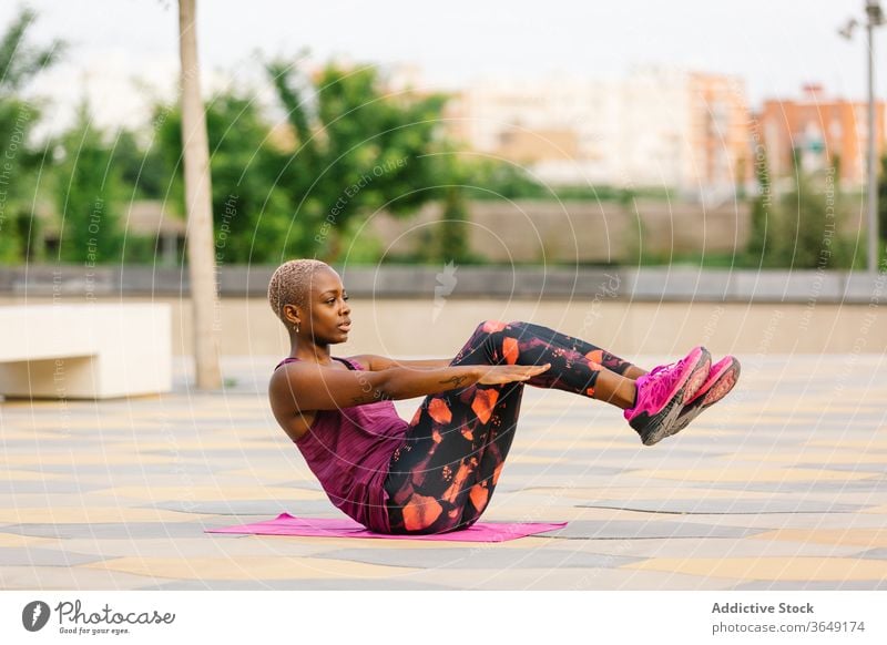 Afroamerikanische Frau sitzt in Half Boat Pose am Damm Halbboot-Pose Yoga üben Gleichgewicht Stauanlage Sportbekleidung Gesundheitswesen Großstadt Handtuch