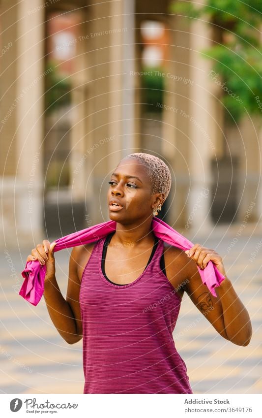 Müde schwarze Sportlerin mit Handtuch steht nach dem Training auf der Böschung Pause Sportkleidung Mund geöffnet müde Gesundheit Gebäude Straßenbelag Großstadt
